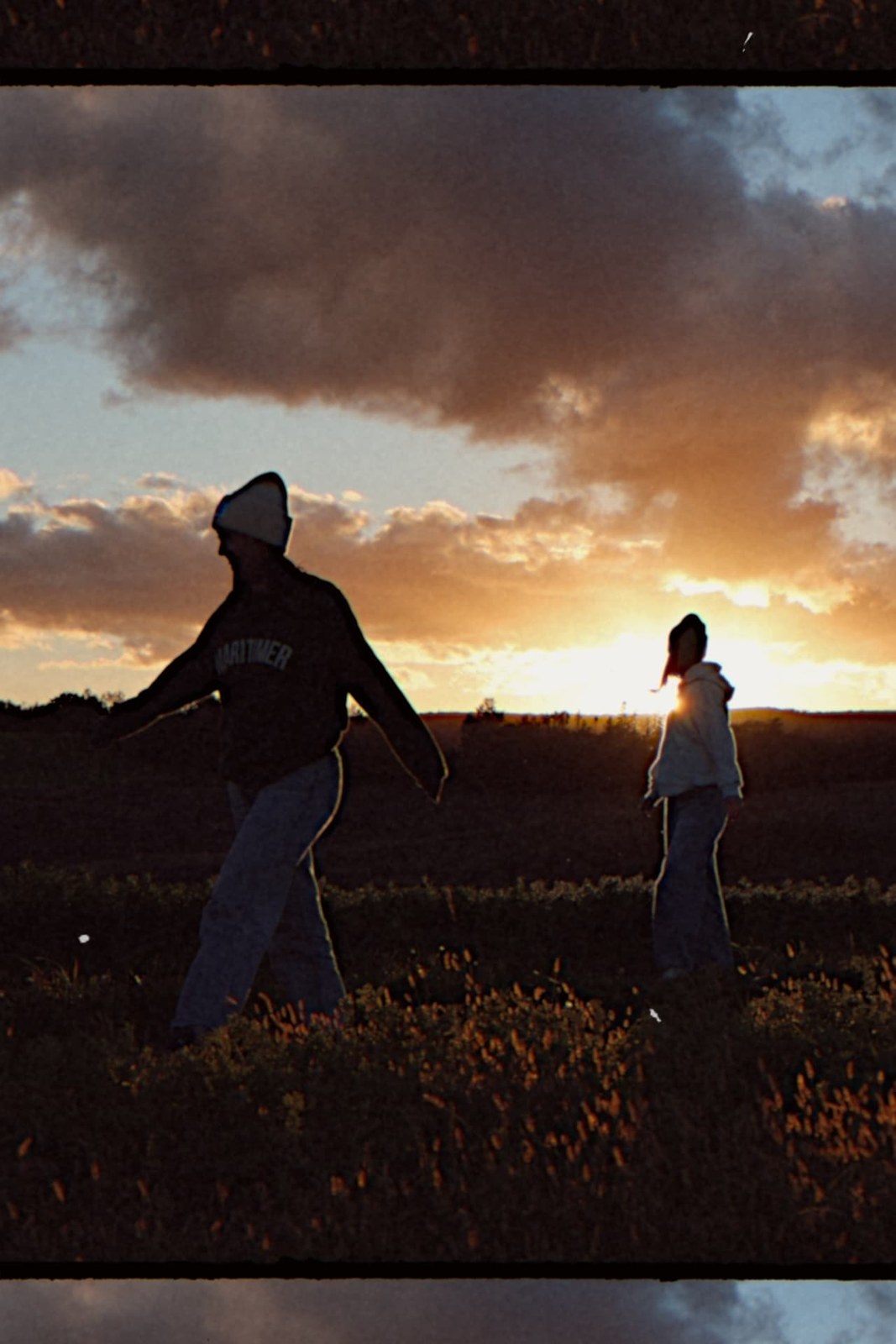 Film-bordered photo of two women walking through a field silhouetted against the sunset
