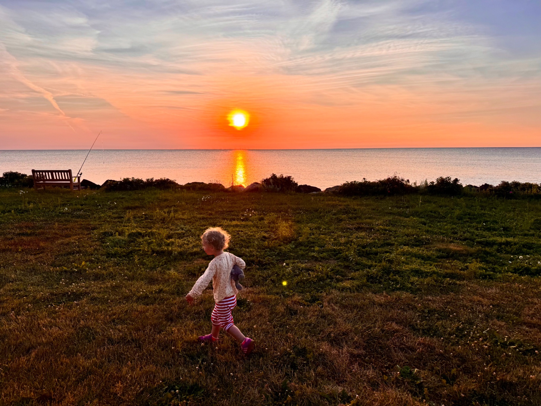 A child running through a grassy field at sunset with the ocean and golden sun in the distance