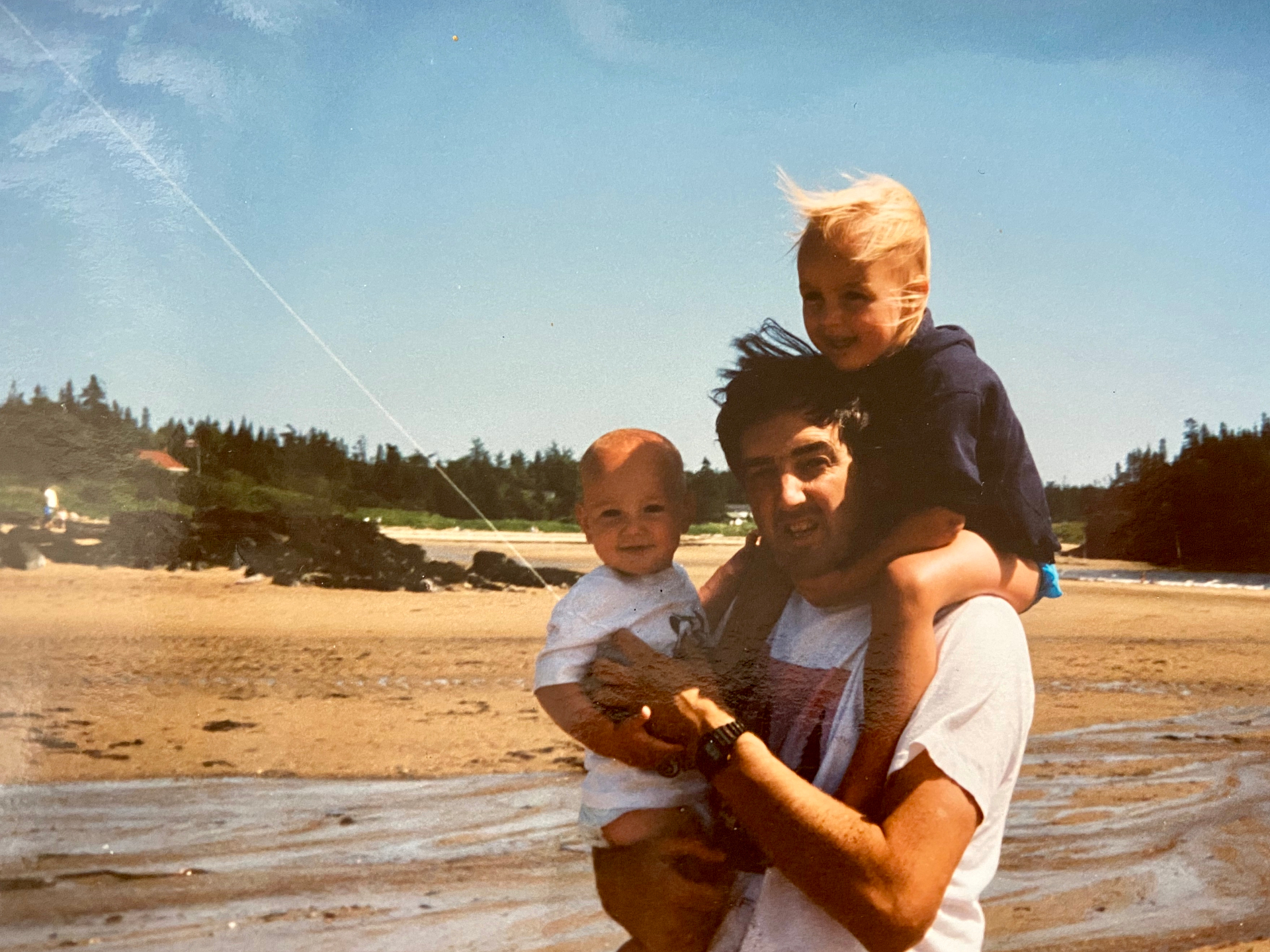 A father on the beach in New Brunswick holding his two young kids